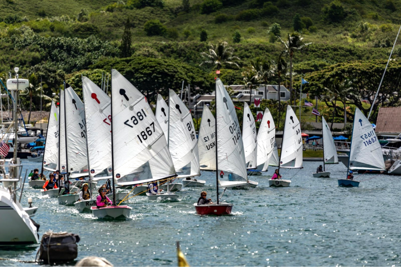 A large number of 8 foot El Toro sailboats with Junior sailors leaves the harbor at Kaneohe Yacht Club.