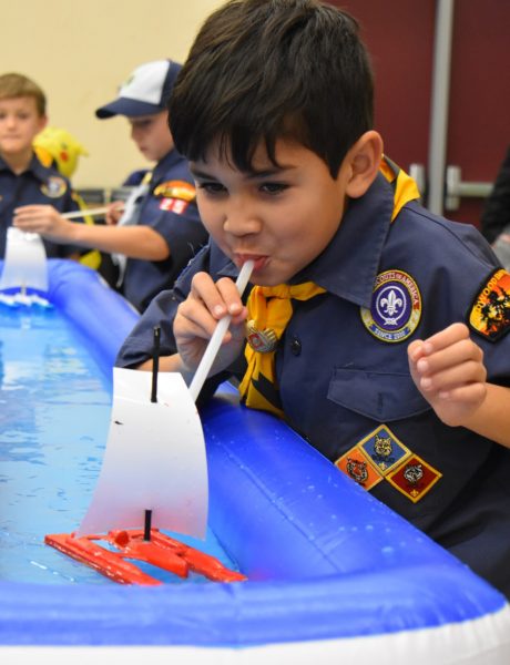 Cub scout using straw to blow his trimaran