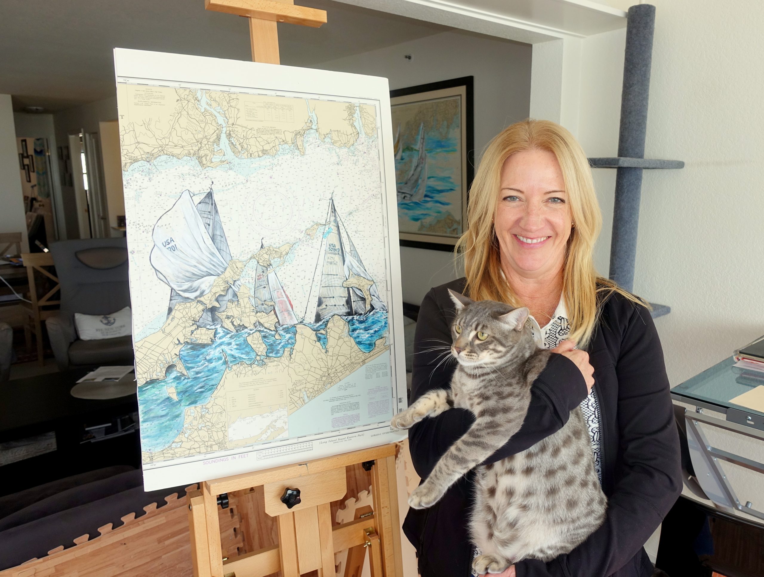 Denise Kramer stands by her painting, holding her cat.