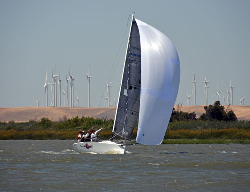 Melges 24 racing under spinnaker with windmills in the background.