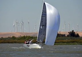 Melges 24 racing under spinnaker with windmills in the background.