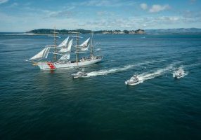 The U.S. Coast Guard Cutter Barque Eagle (WIX-327) and three 47-foot Motor Life Boats sail past the Cape Disappointment Lighthouse, at the mouth of the Columbia River, June 16, 2025. The Eagle departed Astoria, Oregon after a four-day port call. (U.S. Coast Guard photo by Petty Officer 3rd Class Daylan M. Garlic-Jackson)