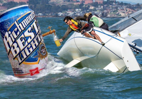 Beer Can Racing poster depicting a sailor leaning over a healed sailboat. He is reaching out to fill a glass beer mug from a spigot on a humungous can of beer floating in the ocean.